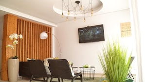A modern living room with a wooden slat wall, a flat-screen TV, a black sofa, a floor lamp, and a potted plant. - Ouril Hotel Julia (Sal)