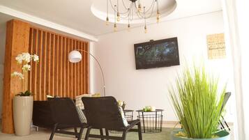 A modern living room with a wooden slat wall, a flat-screen TV, a black sofa, a floor lamp, and a potted plant.