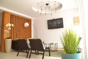 A modern living room with a wooden slat wall, a flat-screen TV, a black sofa, a floor lamp, and a potted plant. - Ouril Hotel Julia (Sal)