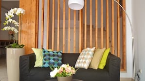 A modern living room with a black sofa, patterned cushions, a white pendant lamp, and a wooden slatted partition. - Ouril Hotel Julia (Sal)