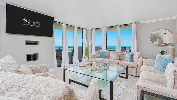 A modern living room with a large flat-screen TV, a glass coffee table, and a sofa set. - Oceanfront Corner - Horizons Condo #1701 (Daytona Beach)