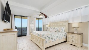 A bedroom with a bed, bedside tables, a ceiling fan, and a view through a sliding door. - Oceanfront Corner - Horizons Condo #1701 (Daytona Beach)