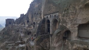 Una estructura histórica de piedra con arcos y escaleras esculpidas en un acantilado.
