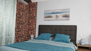 Un dormitorio con pared de ladrillo, una cama con ropa de cama a rayas y un cuadro con una escena de playa.