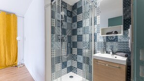 A bathroom with a shower enclosure, a sink, and a mirror.