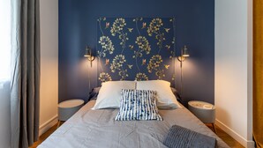 A bedroom with a bed, two bedside tables, a headboard with floral wallpaper, and two wall-mounted lamps.