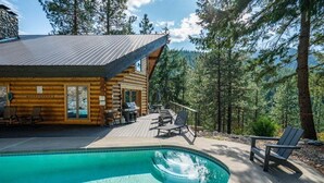 Una cabaña de troncos con piscina, sillas de terraza y vistas al bosque.