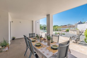 Een buiten eethoek met een tafel voor vier personen, omringd door stoelen, met uitzicht op een tuin en een stenen muur op de achtergrond.