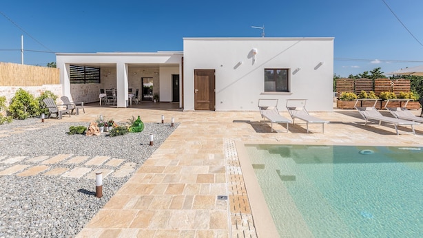 Een modern huis met een zwembad, terras en heldere lucht.