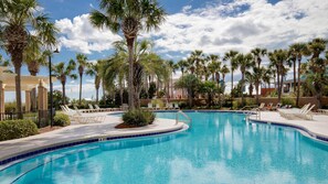 Relax by the serene pool surrounded by lush palm trees and lounge chairs.