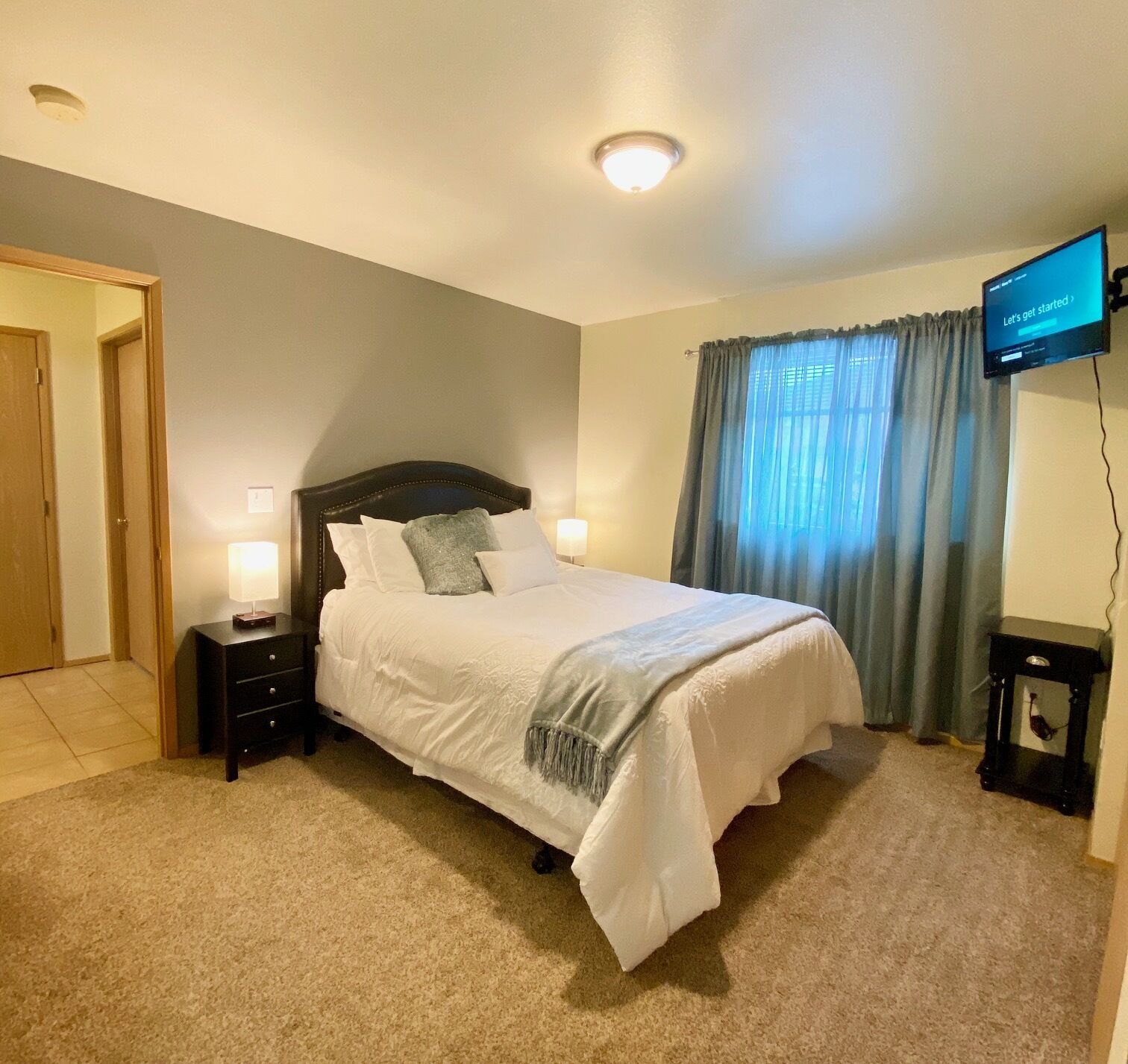 A neatly arranged bedroom with a bed, bedside lamps, a television, and a window with curtains.