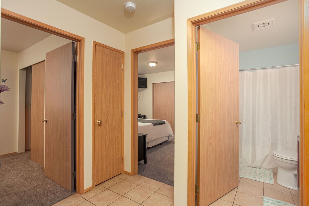 A room with a bed, a bathroom with a shower curtain, and wooden doors.