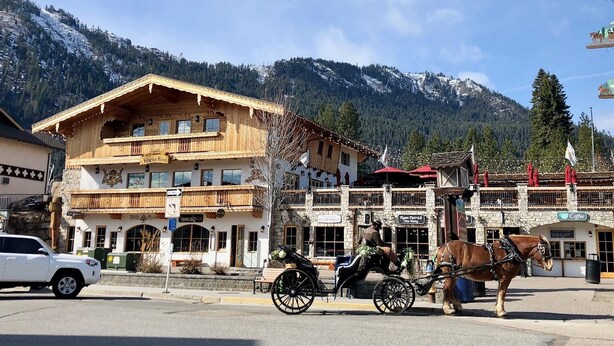 Un edificio de madera con balcones, un carruaje tirado por caballos y un paisaje montañoso de fondo.