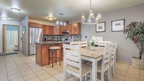 Una cocina moderna con una isla central, armarios de madera y un comedor con sillas blancas.
