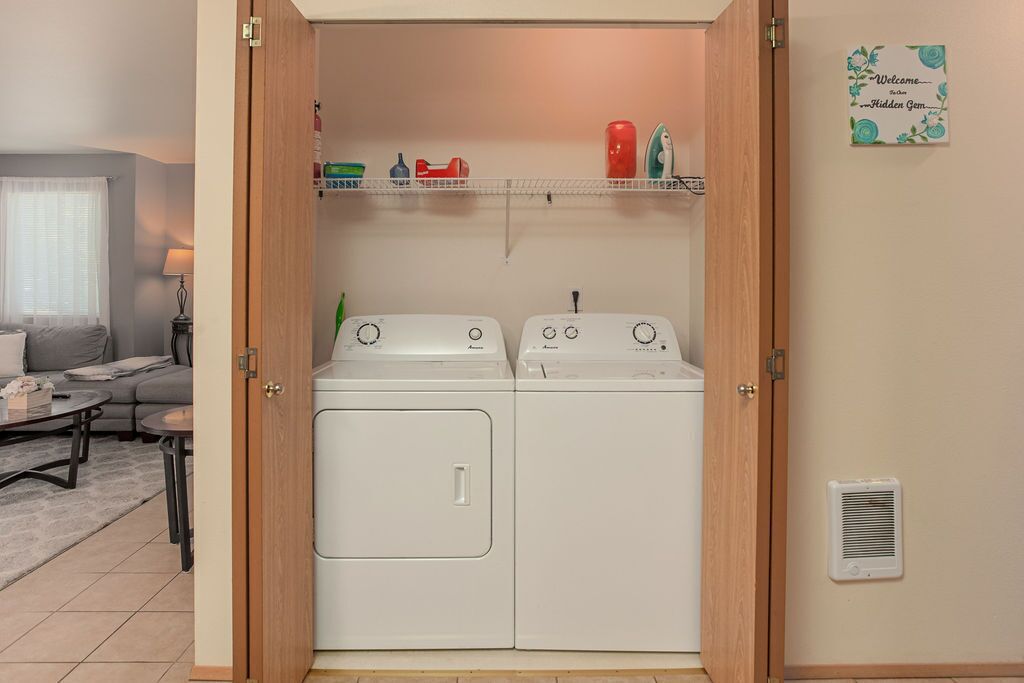 A laundry room with two washing machines and a shelf above.