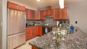 Una cocina con armarios de madera, electrodomésticos de acero inoxidable, una encimera de granito y una lámpara colgante.