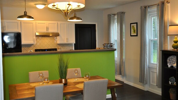 A modern kitchen with white cabinets, a green accent wall, and a dining area with a wooden table and chairs. - Oswego Downtown District (Oswego)