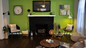 A living room with a green wall, a black fireplace, a mounted TV, and a ceiling fan. - Oswego Downtown District (Oswego)