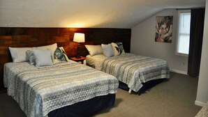 A bedroom with two beds, a nightstand, a lamp, a painting, and a window with curtains. - Oswego Downtown District (Oswego)