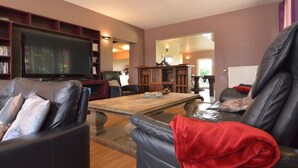 Ein Wohnzimmer mit Fernseher, Ledersofas, einem Holztisch und einem Bücherregal.