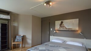 Ein Schlafzimmer mit Bett, Stuhl, Schreibtisch, einem Gemälde und einer Deckenleuchte.
