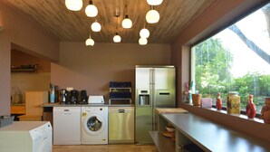 Eine moderne Küche mit Waschmaschine, Geschirrspüler und Kühlschrank. Hängelampen und ein Fenster mit Blick auf Bäume.