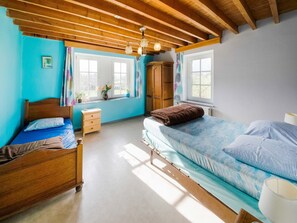 A bedroom with two beds, wooden beams, a window with curtains, and a dresser.
