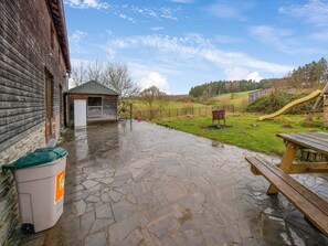 A rustic wooden building with a stone patio, a wooden bench, and a small shed. - Vacation Home with Sauna (Gouvy)