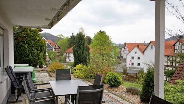A covered outdoor patio with tables and chairs, overlooking a residential area with houses and greenery. - Wohnung mit Eigener Terrasse in Homberg (Homberg)