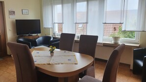 A dining area with a round table, chairs, a television, and windows with curtains. - Wohnung mit Eigener Terrasse in Homberg (Homberg)