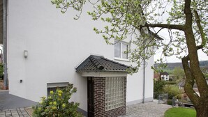 A building with a white exterior, a small brick structure with a tiled roof, and a paved courtyard with a tree and shrubs. - Wohnung mit Eigener Terrasse in Homberg (Homberg)