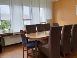 Ein Essbereich mit einem Holztisch, sechs Stühlen, einer Heizung und Fenstern mit weißen Vorhängen.