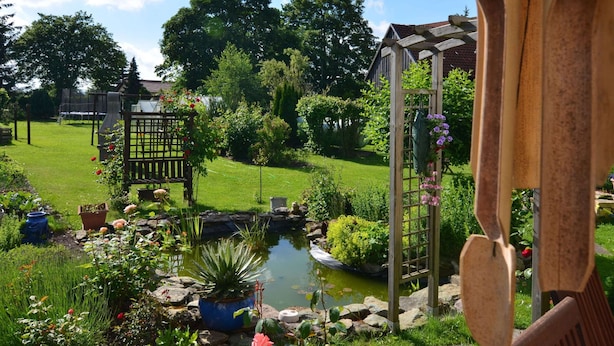 Ein Garten mit Teich, einer Holzpergola und einem eingezäunten Bereich.