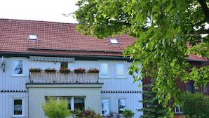 Ein zweistöckiges Gebäude mit rotem Ziegeldach, weißen Außenwänden und einem Balkon mit Blumenkästen.