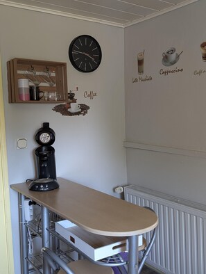 Un área de cocina con cafetera, un reloj y adornos de pared que incluyen ilustraciones y texto relacionados con el café.