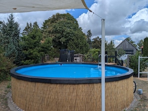 An outdoor swimming pool with a wooden border, surrounded by trees and a wooden structure in the background. - Peaceful Apartment in Hüttenrode near Braunlage Ski Area (Blankenburg)
