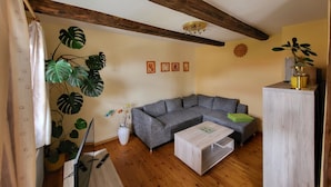 Ein Wohnzimmer mit einem grauen Ecksofa, einem Holztisch und einer Pflanze.