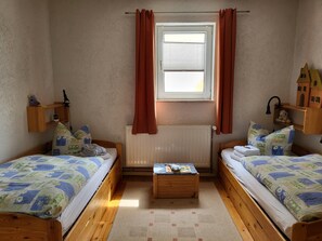 A bedroom with two wooden beds, a radiator, a window with curtains, and a small wooden table with a toy. - Peaceful Apartment in Hüttenrode near Braunlage Ski Area (Blankenburg)