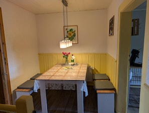 A dining room with a table set for two, a vase of flowers, and a painting on the wall.