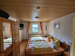 A room with a wooden ceiling, a bed with floral bedding, a window with curtains, and a television on the wall. - Peaceful Apartment in Hüttenrode near Braunlage Ski Area (Blankenburg)