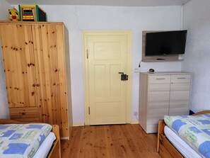 Un dormitorio con un armario de madera, una puerta, un televisor y dos camas.