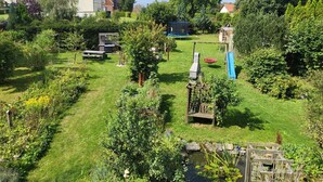 Ein üppiger Garten mit Teich, hölzernen Spielgeräten und einem Trampolin.