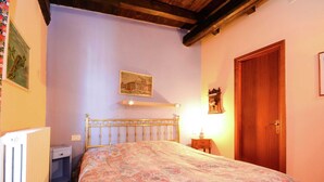 A bedroom with a bed, a wooden door, a nightstand, a wall-mounted lamp, and a radiator. - Belvilla by OYO Casa Reale Quattro (Montecalvo Versiggia)