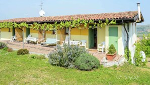 A two-story house with a tiled roof, a covered patio with outdoor furniture, and a garden area with shrubs and flowers. - Belvilla by OYO Casa Reale Quattro (Montecalvo Versiggia)