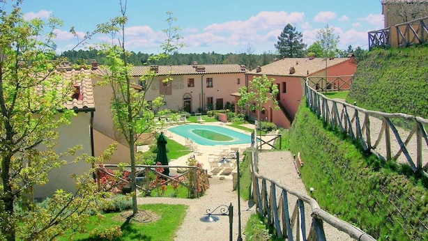 Ein Innenhof mit Swimmingpool, umgeben von Gebäuden mit Terrakotta-Dächern und einer Steinmauer.