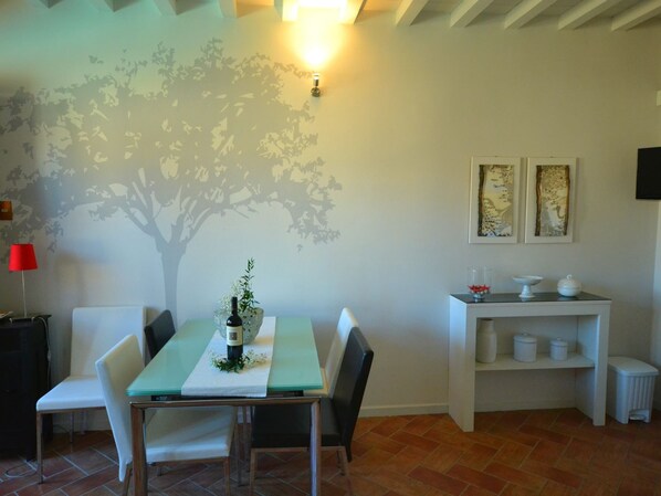 Uma sala de jantar com mesa, cadeiras, uma garrafa de vinho e um mural na parede.