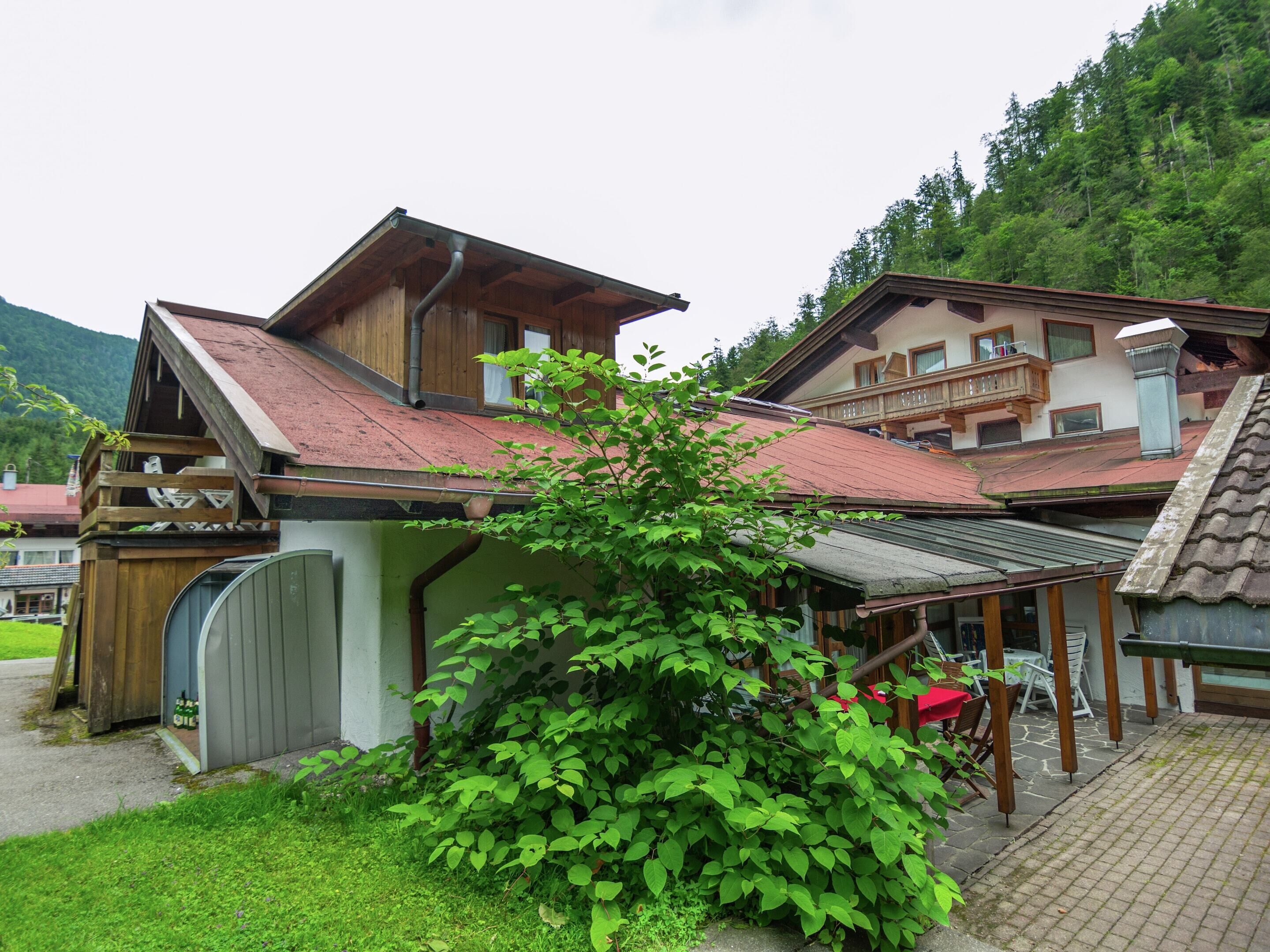 Ein traditionelles Holzchalet mit geneigtem Dach, einer überdachten Veranda und einem kleinen Garten mit einem Busch.