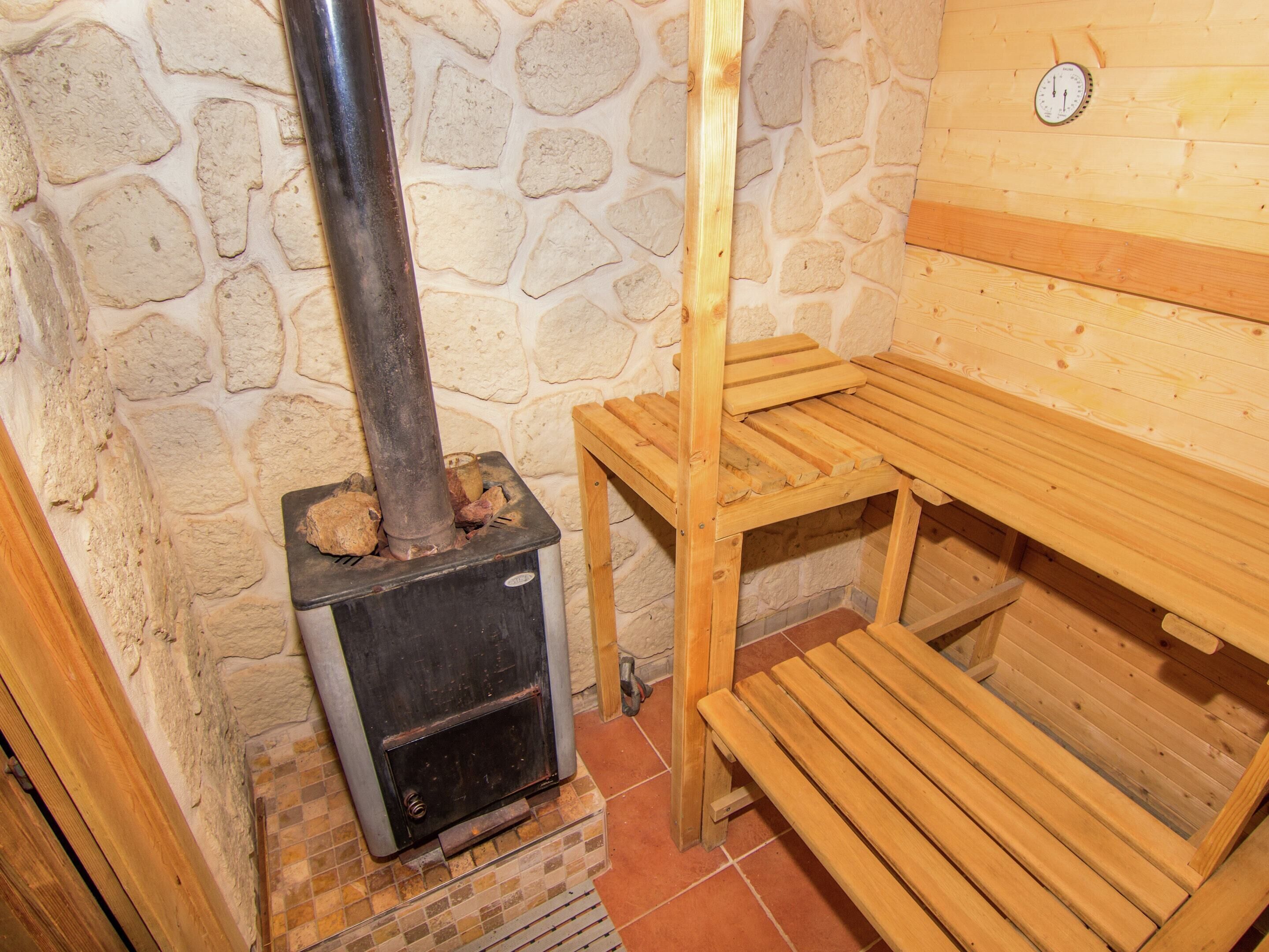 Una habitación con paredes de piedra, un estufa de leña, un banco de madera y una mesa.