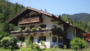 A traditional Alpine-style building with a balcony, a sign indicating it is a guesthouse, and a mountainous backdrop. - Ferienwohnung in Ruhpolding (Ruhpolding)