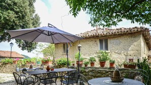 An outdoor patio with stone flooring, metal tables and chairs, potted plants, and a stone building with a tiled roof. - Holiday Home Monte Santa Maria Pool Retreat (Monte Santa Maria Tiberina)